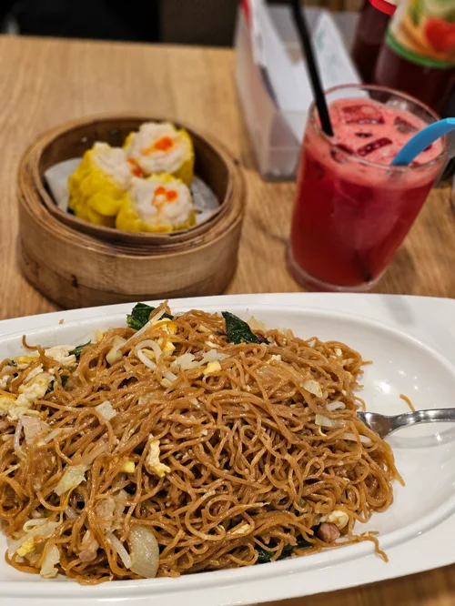 흰 접시에 담긴 볶음면과 뒤쪽 딤섬 찜기