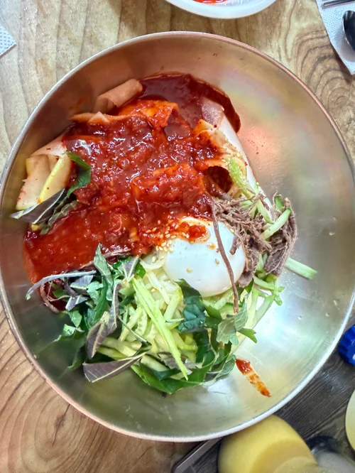 스테인리스 대접에 고추장 양념과 채소, 달걀이 담긴 비빔냉면