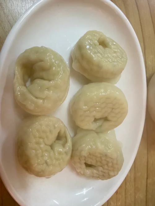 흰 접시에 담긴 연두빛 반투명 피의 찐만두 5개