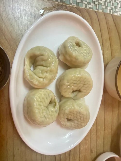 흰 타원형 접시에 담긴 5개의 윤기 있는 찐만두