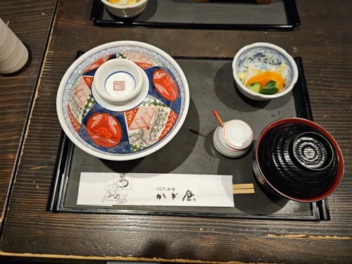 검은 쟁반 위에 전통 문양 뚜껑 그릇과 반찬이 세팅된 일본식 상차림